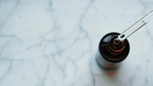 Brown Bot tles of essential oil. Top view. Drop falls from a pipette into a cosmetic bottle. Hair care, drop of oil restore and recovery. cosmetic amber bottle. Mramor background with copy space