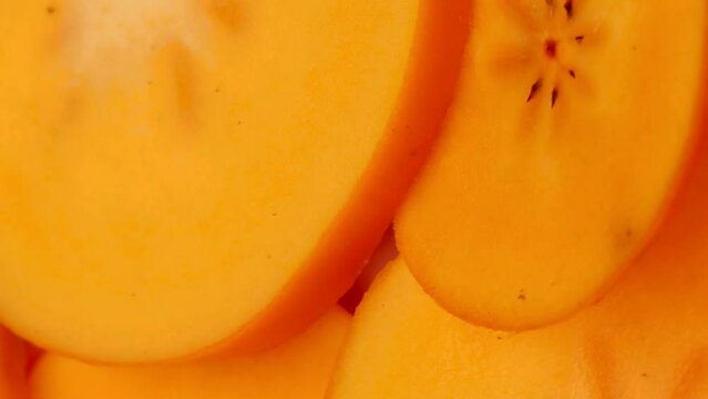 Slices of persimmon, rotating in a circle. Fresh orange persimmon (kaki), turning. Cut persimmon fruits. Selective focus. vertical video