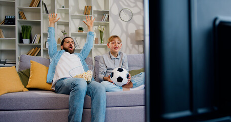 Man and boy watching football sports games on TV and reacting happy exiting when team Shoot the...