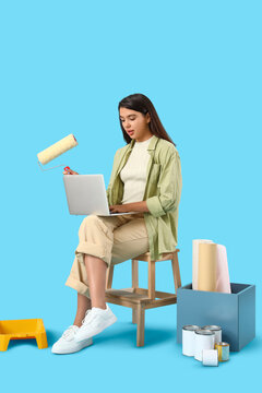 Young woman with paint roller and laptop on blue background