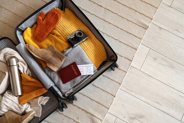 Open suitcase with travelling accessories and winter clothes on carpet, top view