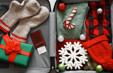 Open suitcase with winter clothes and Christmas gift on floor, top view