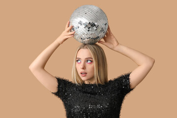 Naklejka premium Beautiful thoughtful young woman with disco ball on brown background