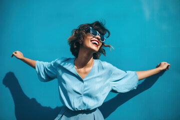 Young fashionable woman wearing sunglasses and dancing in front of blue wall