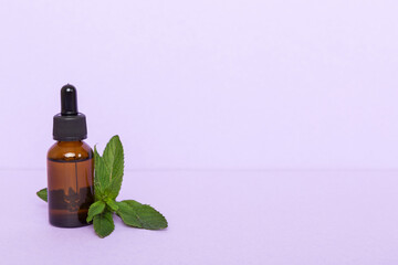 Natural Mint Essential Oil in a Glass Bottle. organic cosmetics with herbal extracts of mint on colored background