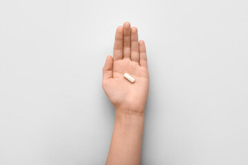 Naklejka premium Female hand with white capsule on light background