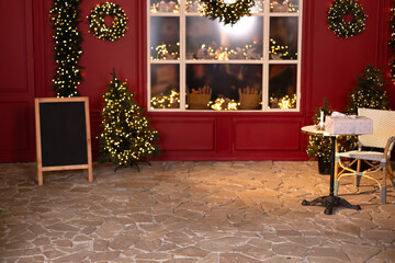 Christmas trees with lights garlands, store window. Red decorated coffee house for christmas.  Xmas cafe terrace with table and chair. Cozy outdoor cafe on Xmas. New Year's decorations of the street. 