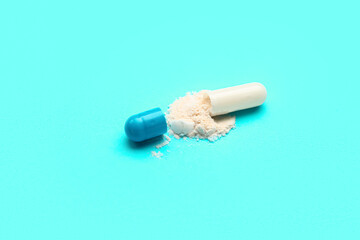Opened capsule with powder on blue background, closeup