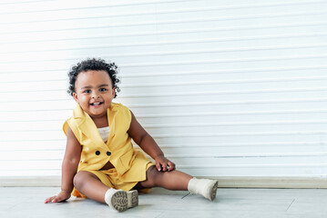 Portrait images, A 2-year-old Nigerian baby girl with beautiful curly hair, sitting on the floor, is smiling broadly.  to African baby girl