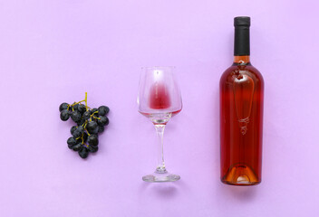 Glass and bottles of exquisite wine with grapes on lilac background