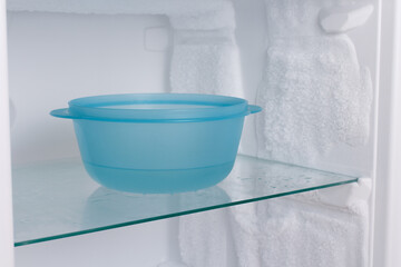 Blue plastic bowl of water on a glass shelf in the freezer.