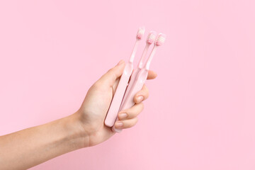 Female hand with three pink toothbrushes on pink background.