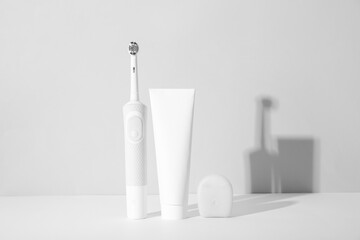 Electric toothbrush with toothpaste and dental floss on white background.