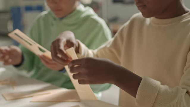 Chest up of inquisitive African American schoolboy woodworking at desk in classroom with classmate