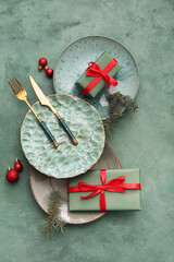 Beautiful table setting with Christmas balls, fir branches and gift boxes on green background