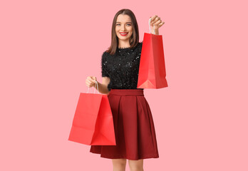 Young woman holding shopping bags on pink background