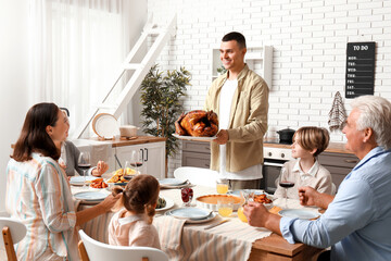 Young man bringing turkey at festive table with his family on Thanksgiving Day