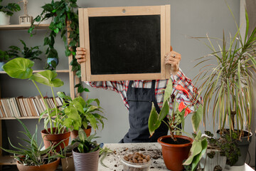 Young male florist holding black board in home greenhouse