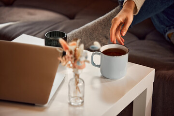 Fototapeta na wymiar Woman's delicate hand reaches for cup of hot fragrant tea standing on coffee table at home. Relaxing atmosphere. concept of lifestyle, winter holiday season, autumn weekend, relax and cozy.