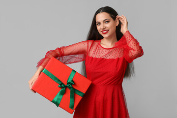 Beautiful young woman with Christmas gift on grey background