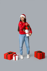 Beautiful young woman in Christmas sweater with gift boxes on grey background
