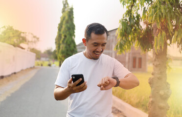 Asian man checking his smart watch after doing outdoor workout on the street in afternoon