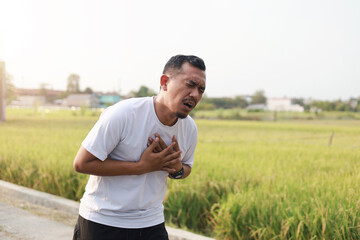 Asian athlete suffering from chest pain while running, heart aches after cardio exercise