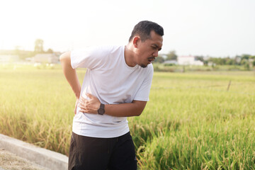 Asian man with her muscle pain during running. Runner man having back and waist body ache due to Piriformis Syndrome, Low Back Pain and Spinal Compression. Sports injuries and medical concept - obrazy, fototapety, plakaty