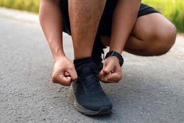 Adult Asian man tying his shoelaces and getting ready to go jogging and exercising outside - obrazy, fototapety, plakaty