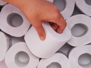 A person hand taking a toilet roll from heap of toilet paper rolls. Close-up