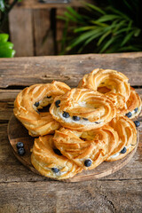 Choux rings with cream and blueberry. Wooden background, side view. 