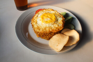 Indonesian style spicy fried rice with shredded chicken, cucumber pieces and tomato pieces and fried eggs and shrimp crackers.
