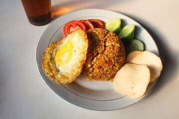 Indonesian style spicy fried rice with shredded chicken, cucumber pieces and tomato pieces and fried eggs and shrimp crackers.
