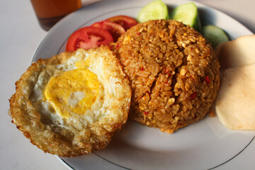Indonesian style spicy fried rice with shredded chicken, cucumber pieces and tomato pieces and fried eggs and shrimp crackers.