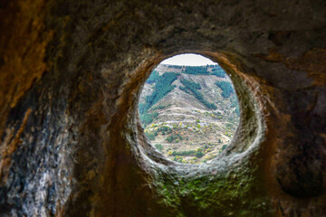 A round window in a sandstone cave with a view of the opposite mountain. Selective focus