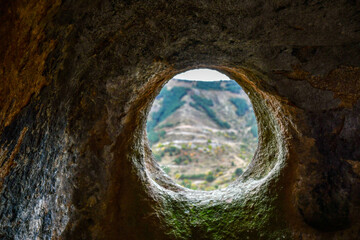 A round window in a sandstone cave with a view of the opposite mountain. Selective focus