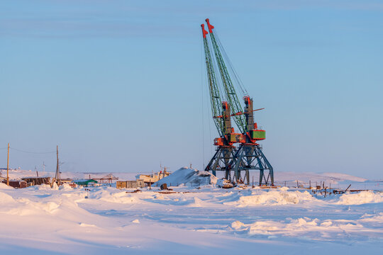 View of the port cranes on the pier among the ice and snow. Winter industrial landscape. Transport infrastructure in Siberia and in the Far North of Russia in the Arctic. Anadyr, Chukotka, Russia.
