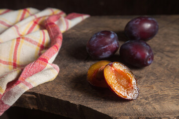 Whole and half of purple plums on wooden background. .