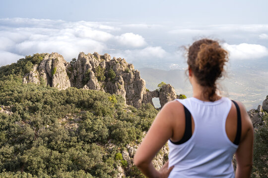 A young caucasian brunette woman from behind out of focus looking at the mountain landscape "La finestra de la Safor" and a sea of clouds