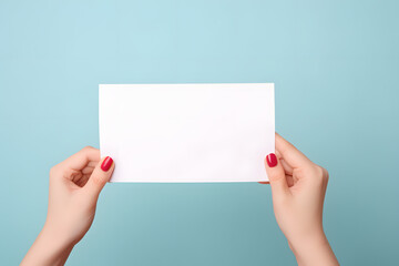 Woman's hands holding up white empty paper note in front of blue background - obrazy, fototapety, plakaty