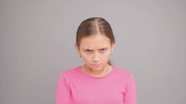The girl lowers her head and gets angry. Portrait of a child in a pink sweater on a gray background.