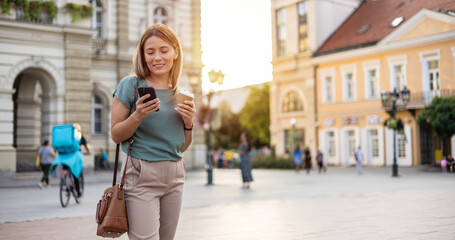 Cropped shot of an attractive young woman standing outside on the street and using her cellphone to...