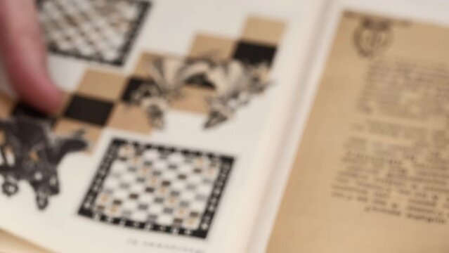 a man in a blur is studying a chess tutorial. a person flips through the pages of a book with illustrations to study the chess game. visual aid. closeup.
