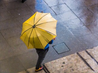 Person walking in the city with yellow umbrella on rainy day