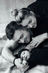 A man and woman cuddle while holding a baby. A Loving Family Moment: Man, Woman, and Baby Cuddle in Warm Embrace