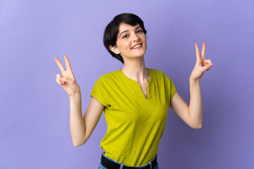 Woman with short hair isolated on purple background showing victory sign with both hands