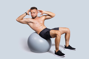 Obraz premium Calm muscular millennial european man with beard, naked torso make exercises with fit ball for abs