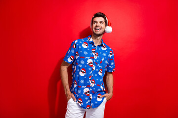 Portrait of satisfied cool person dressed santa hat blue shirt look at discount empty space isolated on vibrant red color background