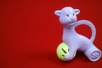 A toy shaped like an alpaca animal, purple color, holding a ball. on a red background