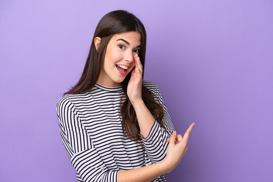 Young Brazilian woman isolated on purple background pointing to the side to present a product and whispering something